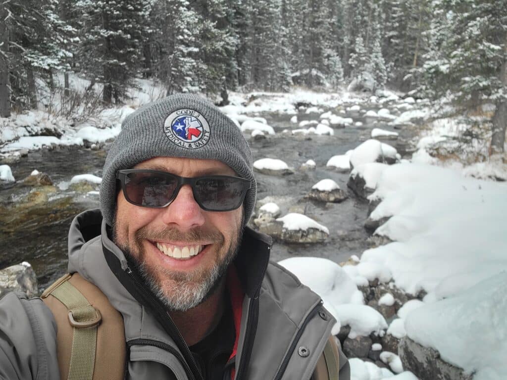A man smiles for a selfie in a snowy forest