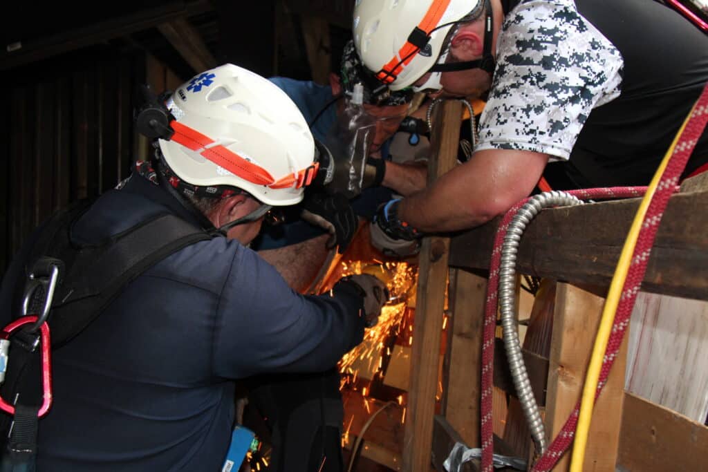 Two firefighters cutting through wood with a saw, sparks flying.