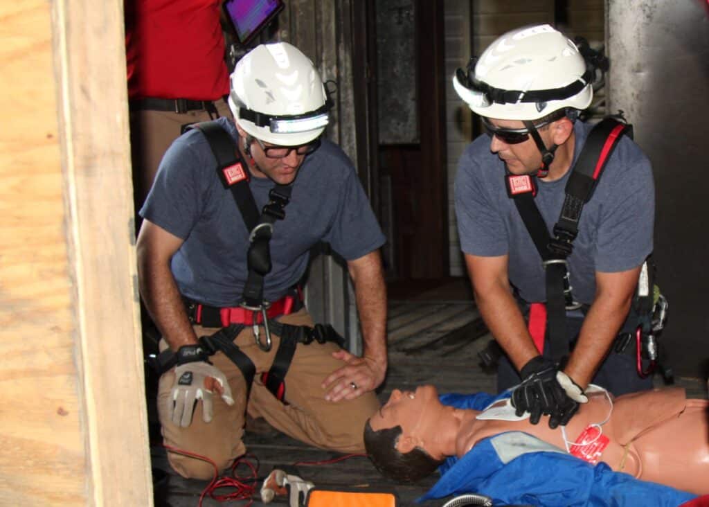 Two individuals in safety gear practicing CPR on a dummy.