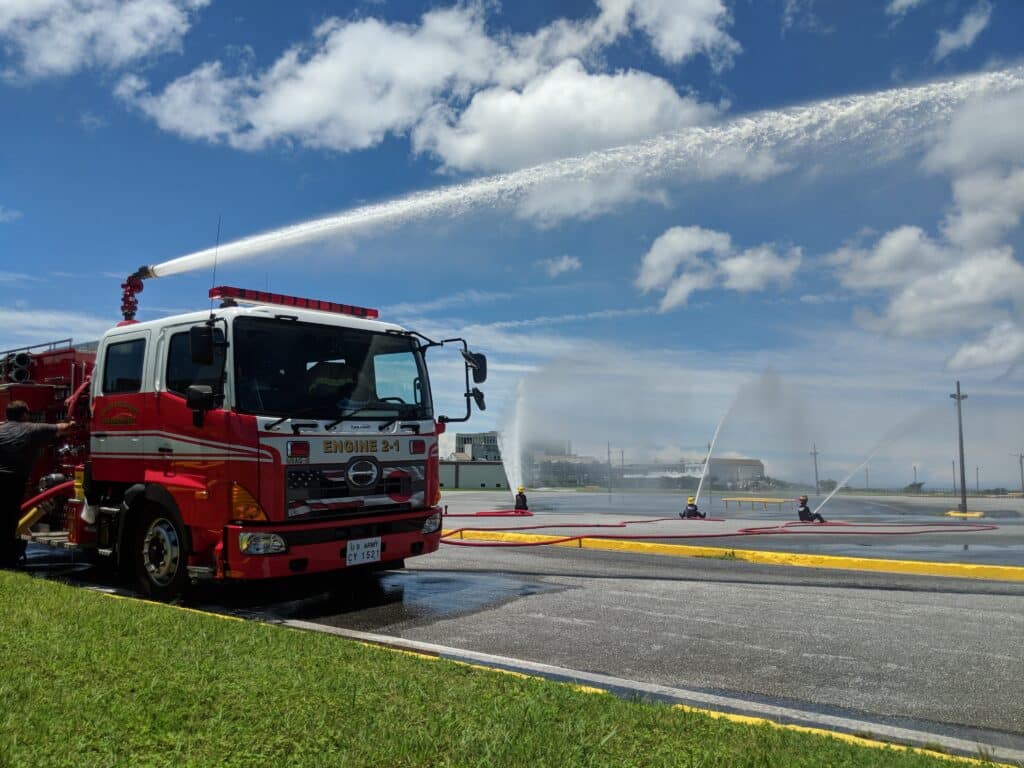 Firetruck sprays water during a demonstration against a blue sky with clouds.