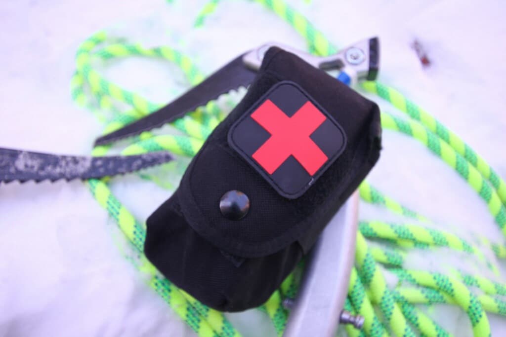 Black pouch with red cross beside climbing rope and carabiner