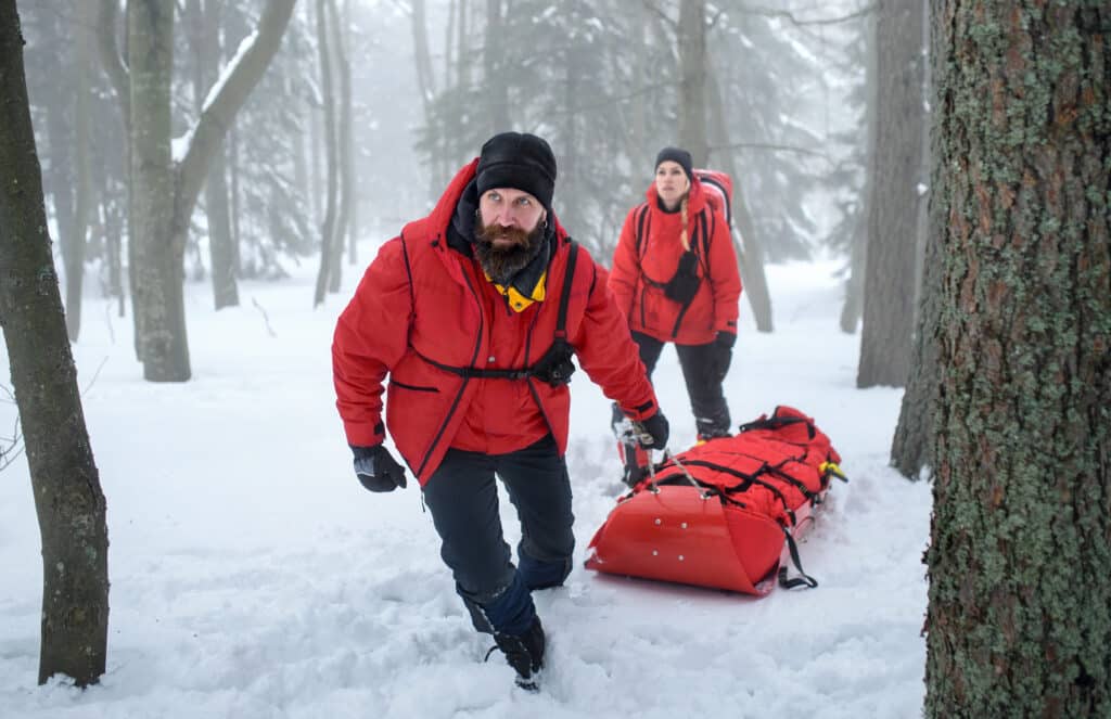 Two people in red jackets pulling a sled through a snowy forest.